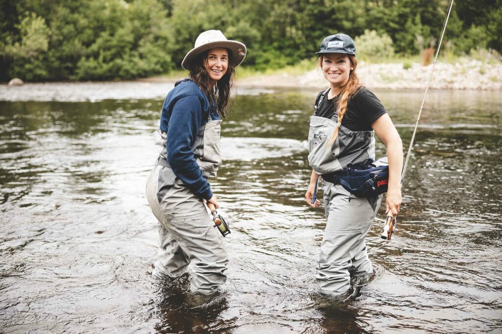 Two women walking in swallow water about knee-high holding fishing poles