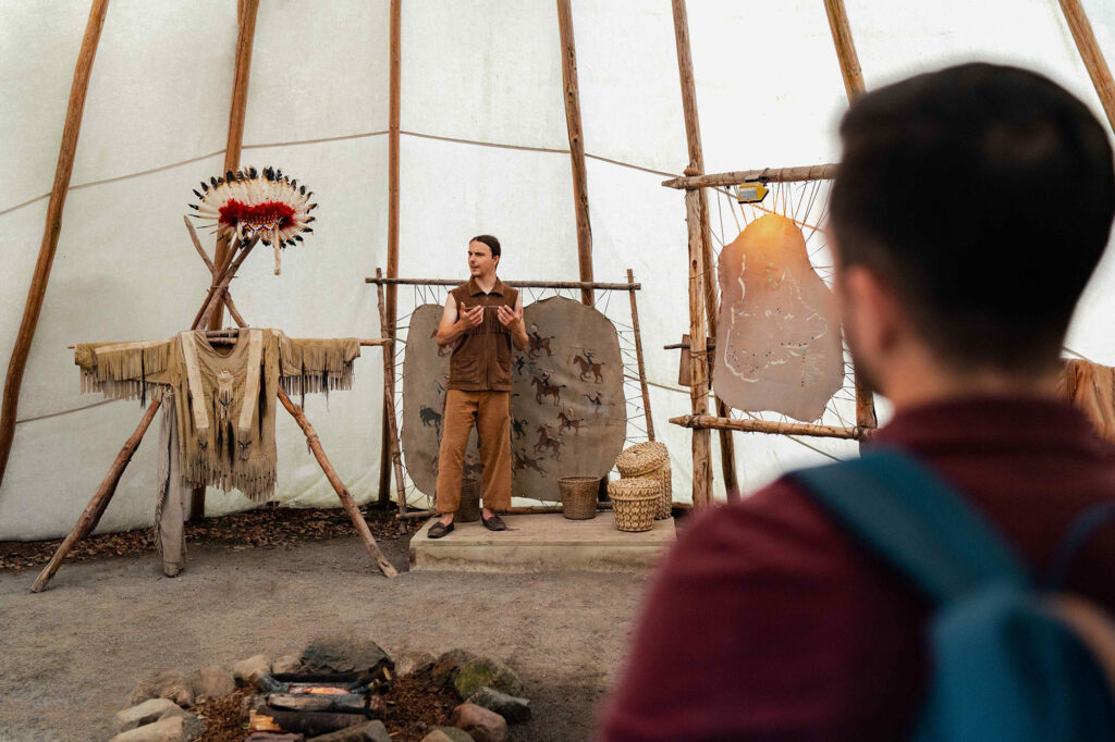 Man standing on a wooden platform in an Indigenous heritage site. He appears to be giving a presentation