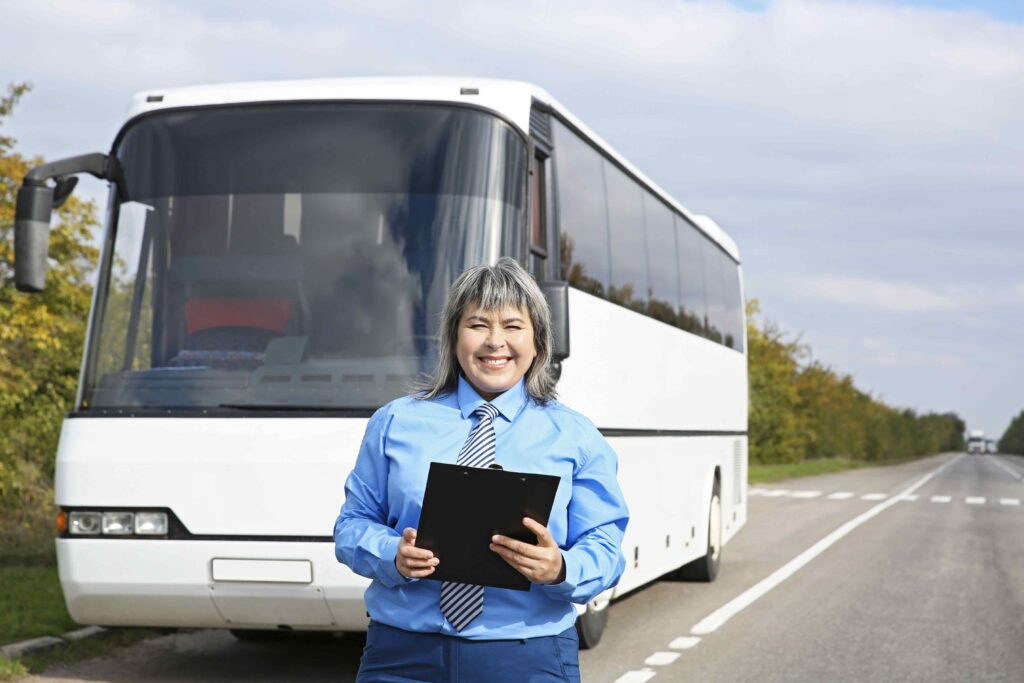 Person smiling while holding a clipboard. Person is standing in front of a white bus. 