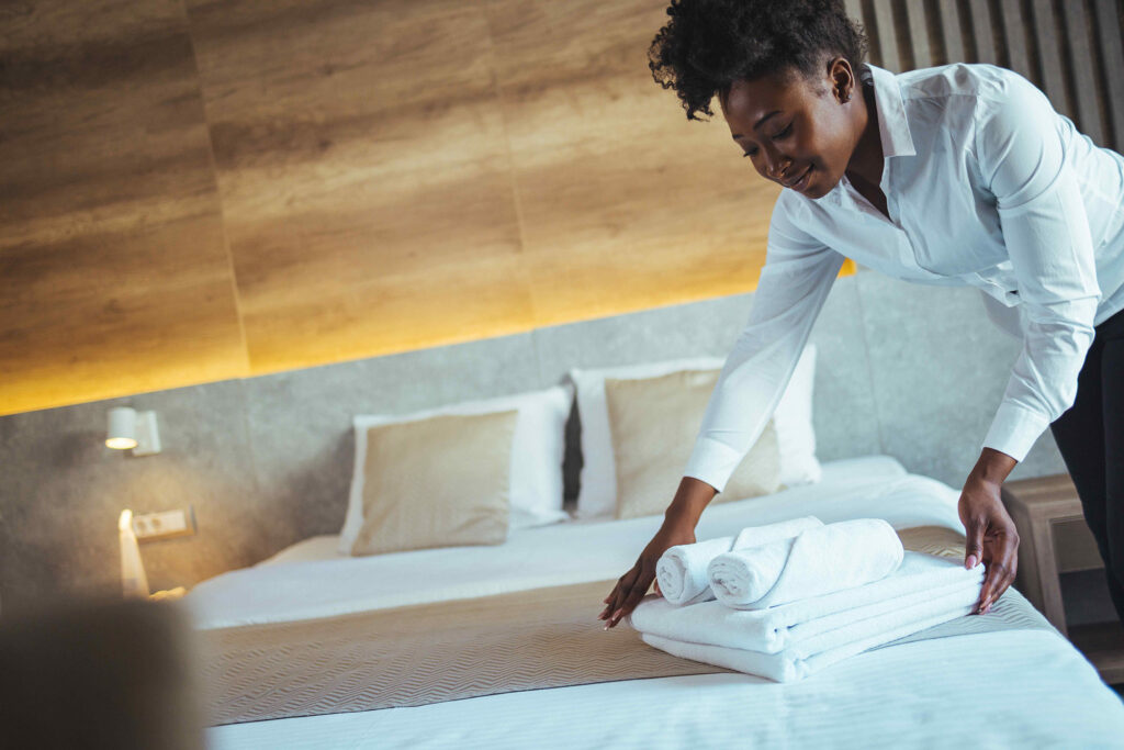 Une préposée à l'entretien dépose des serviettes et des draps propres sur un lit fraîchement fait.