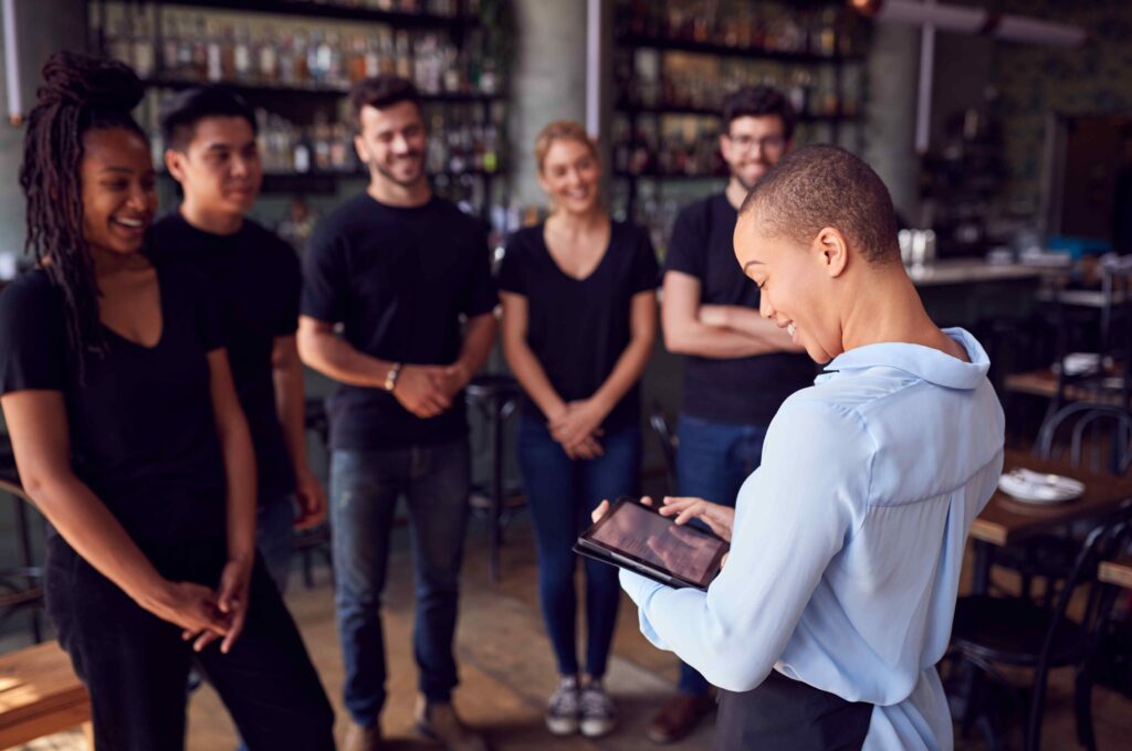 Une directrice de restaurant tient une tablette numérique tout en discutant avec le personnel de service.