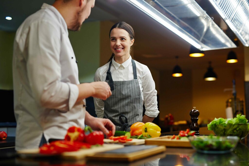 Chef explaining a dish to a kitchen helper as they prepare a meal.