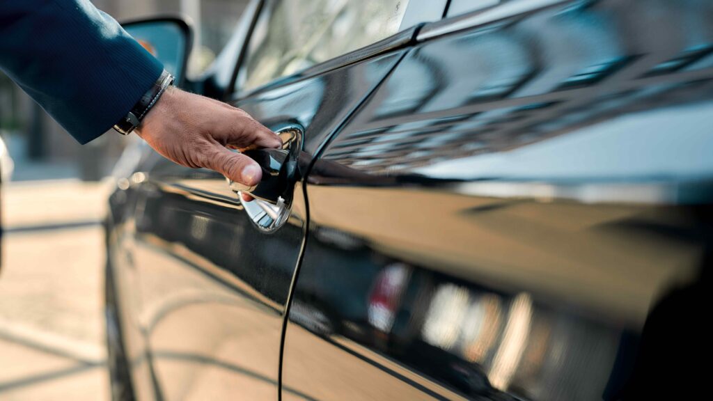 Une personne prend la poignée d'une portière d'une limousine noire.