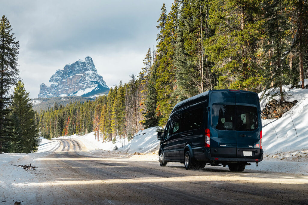 Tour van driving down a road in winter heading towards a mountain in the distance.