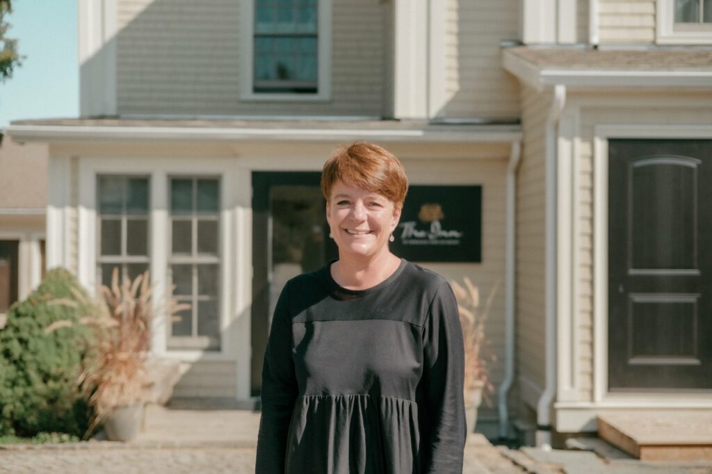 Smiling person standing proudly in front of their small hotel.