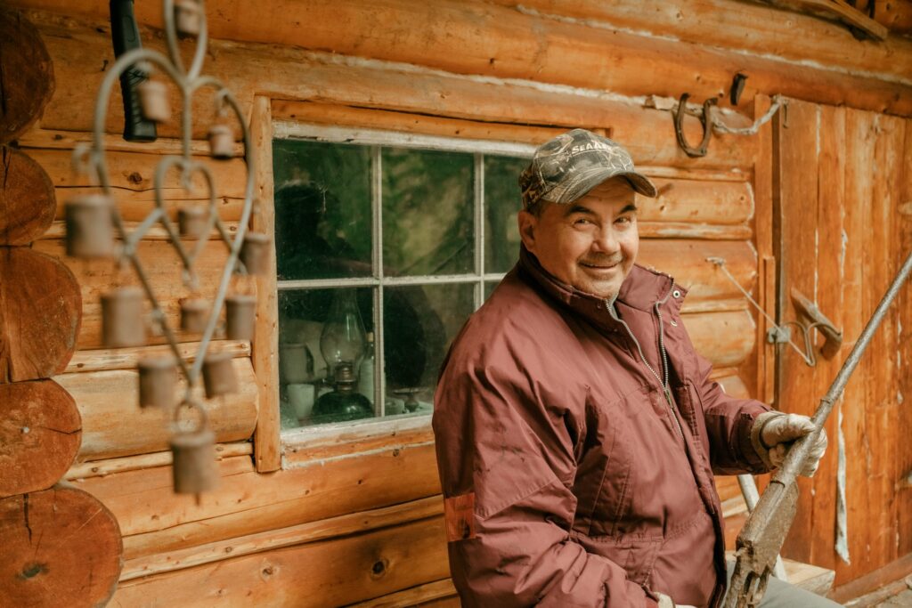 A hunter smiling at a the camera in front of a rustic cabin.