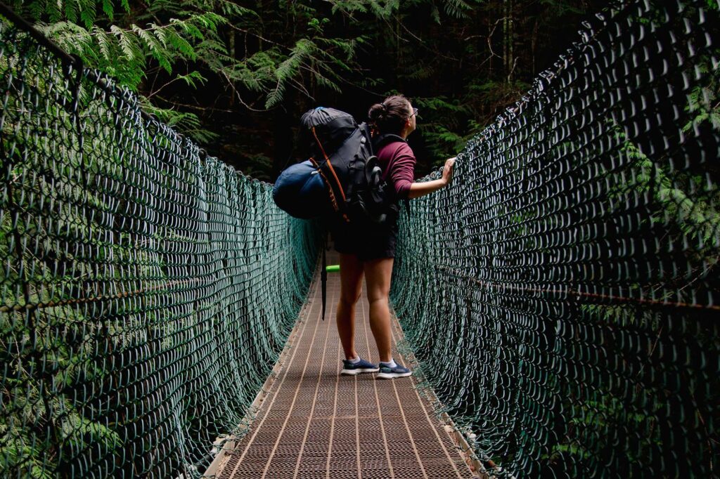 Person with a hiking pack on a suspension bridge traveling through a rainforest.