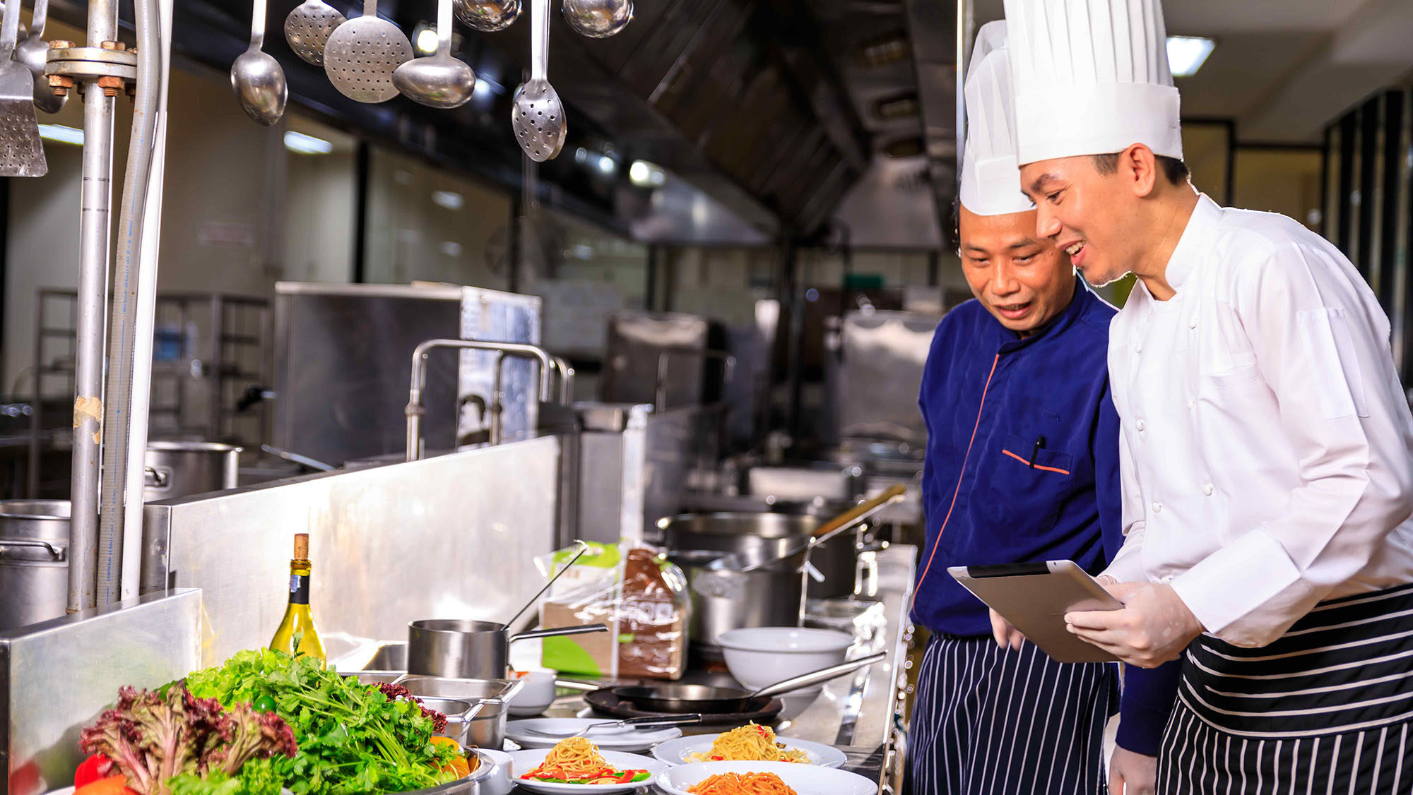 Two chefs standing and admiring several dishes laid out on kitchen table.