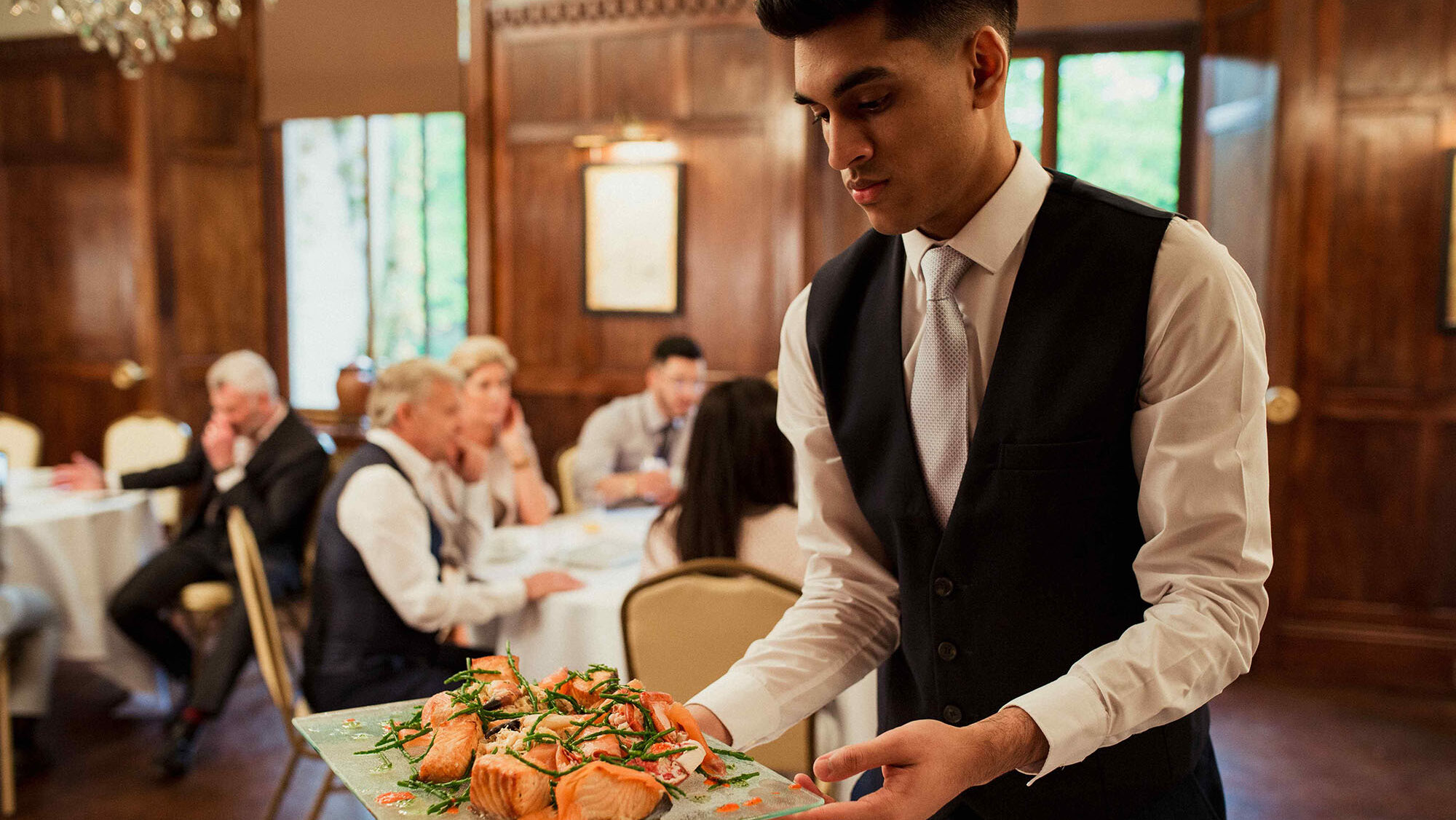 Banquet server placing a plate of food on a table at an event.