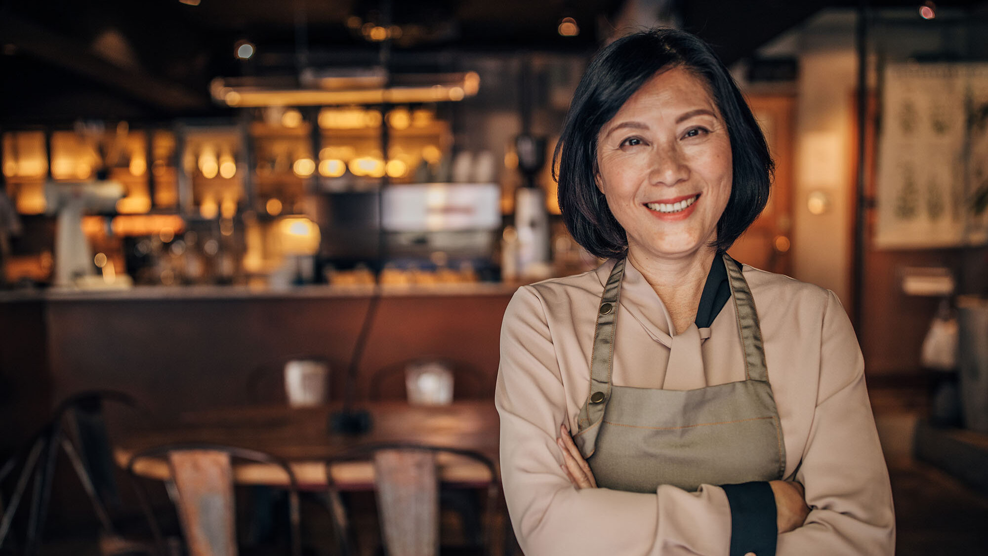 Restaurant owner standing arms crossed in front of a dining area. 