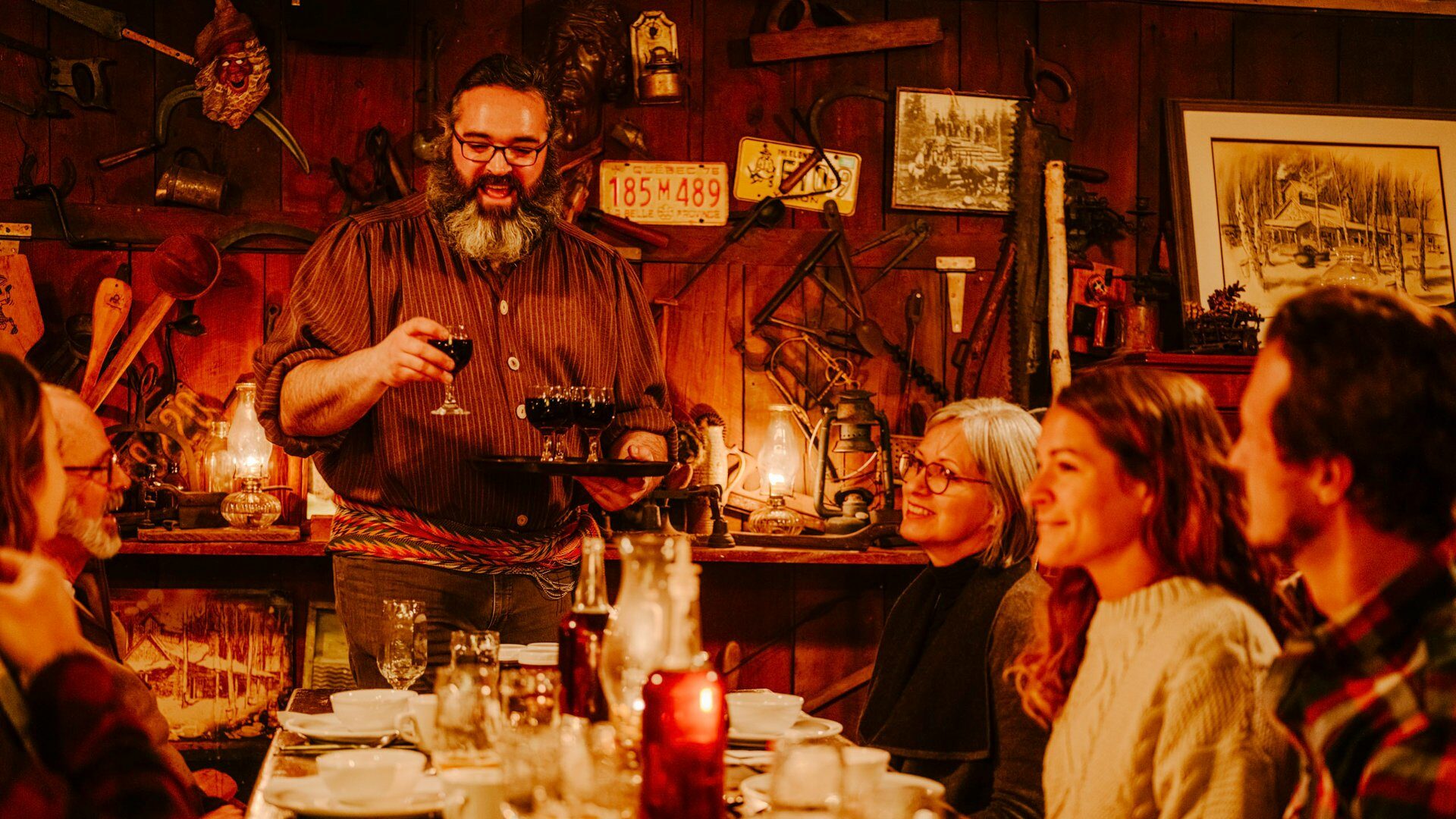 Person serving a tray of drinks to a cozy table of restaurant patrons in an eclectic eatery.